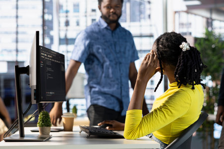 Programmer doing software debugging, asking for help from coworker, checking errors in lines of...