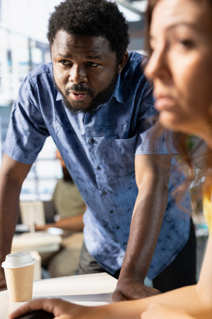 Manager checking paperwork done by employee is in order, looking at computer screen. Supervisor looking over every office PCs to verify workers managed to finish project tasks in timeの写真素材
