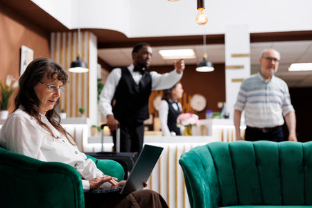 African american bellboy helps senior man with suitcase in modern hotel reception while elderly lady...
