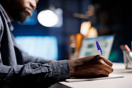Economy specialist writing revenue and cost elements on paper, working from home to create beneficial capital funds investment for global development. African american man analyzing startup budget.の写真素材