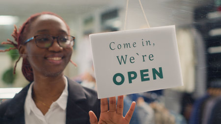 African american worker opening stylish fashion boutique, starting her shift in the morning. Employee turning closed sign on fast fashion clothing store into open one, close up shotの写真素材