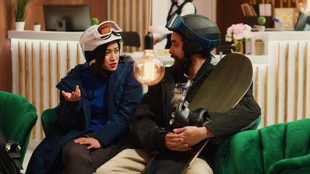 Man tourist giving cash tip to bellboy after serving cups of coffee from ski resort bar, diverse people getting ready to practice winter sports. Couple enjoying hot drink and getting warm in lobby.の写真素材