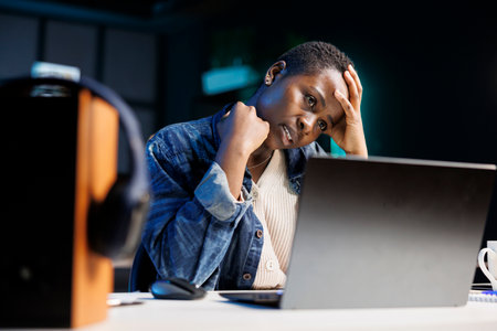 African American female freelancer looking stressed and frustrated as she uses her laptop. Black woman working at home appears tired and exhausted with headache while she browses on personal computer.の写真素材
