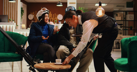 Guests sharing impressions about slope condition after successful skiing and snowboarding practice on slopes, sit in lounge area with sport equipment. Man and woman travelling at alpine resort.の写真素材