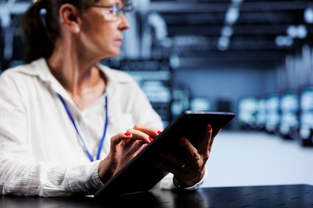 Trained serviceman using tablet to assess server security blips arising due to unsecured network connections. Qualified repairman ensuring data center is impenetrable by malware attacksの写真素材