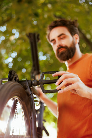 Vibrant sporty caucasian male fixes bicycle components with professional work tool from home yard. Active enthusiastic man outdoors repairing bike crank arm and pedal.の写真素材
