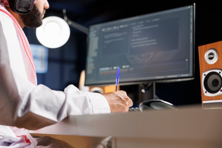 Middle Eastern software developer coding on a laptop to demonstrate the foundations of software development. While using wireless headphones, an Arab guy runs algorithms. Close-up shot.の写真素材