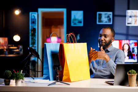 African american content creator filming vlog, unboxing bags with internet order, showing subscribers purchases he recently got. Fashion enthusiast presenting fans shopping acquisitionsの写真素材