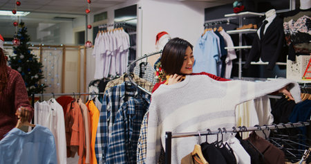 Smiling client in Christmas ornate fashion shop looking to purchase comfortable clothes on clearance, taking advantage of reduced prices during holiday season promotional salesの写真素材