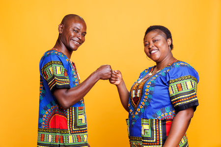 Smiling african american couple making fist bump and looking at camera with cheerful expression. Carefree man and woman showing greeting gesture portrait on orange backgroundの写真素材