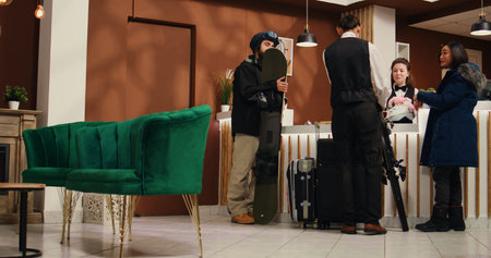 Young people with luggage and gear getting room reservation for wintertime vacation at alpine ski...