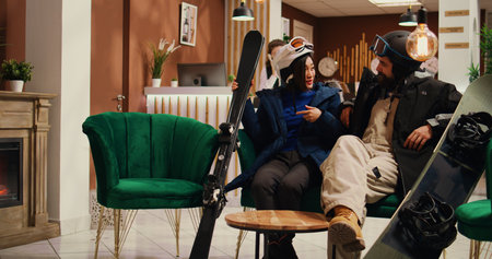 People sitting in lounge area with sliding gear, preparing to go skiing down slopes. Active man and woman checking their equipment to go practice winter sports at mountain resort.の写真素材
