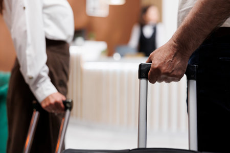 Close-up of a caucasian couple with bags entering foyer of a luxury hotel. View of retired senior customers holding bags as they approach the registration counter to check in with receptionists.の写真素材