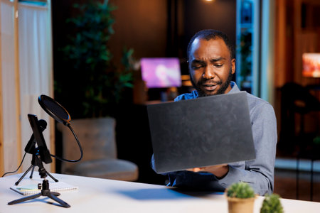 BIPOC content creator filming tech tutorial on how to repair water damaged laptop, presenting internal components. Technology guru in home studio teaching subscribers to install operating systemの写真素材
