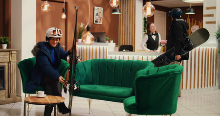 Asian person preparing to go sliding and sitting in lounge area at mountain ski resort, checking skis gear and headgear. Winter sport fan getting equipment ready for skiing down slopes.の写真素材