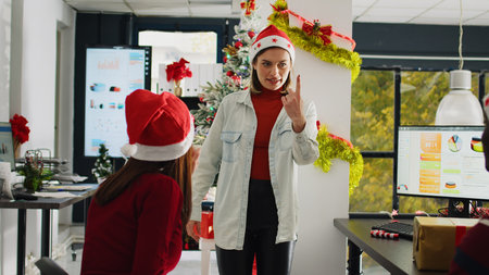 Employees wearing Santa Claus hat enjoying Christmas spirit mood playing pretending acting game during break. Coworkers having fun trying to guess actions during pantomime in xmas adorn officeの写真素材