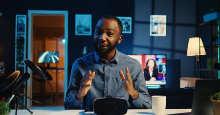 Tech content creator filming unboxing of newly released gaming VR glasses for audience in neon illuminated home studio. BIPOC internet star offers virtual reality headset recommendation to subscribersの写真素材