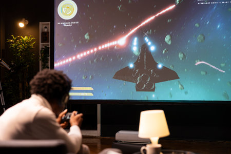 Man in home theatre using cloud gaming service to play demanding SF videogame on projector screen....