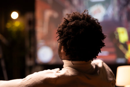Focus on gamer in front of smart TV in blurry background, watching videogame gameplay from content creator. Man in home theatre enjoying gaming content online published by professional streamerの写真素材