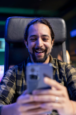Cheerful male individual grasping his mobile device, chatting online with friends and family. Excited young man surfing the net on his cell phone, looking at funny content on social media.の写真素材
