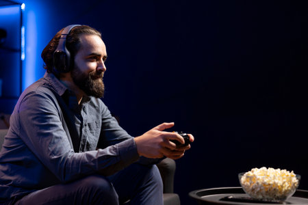 Smiling man focused on defeating enemies while playing videogames on gaming console with teammates. Cheerful player fights foes in esports game using gamepad, chatting with friends through headsetの写真素材