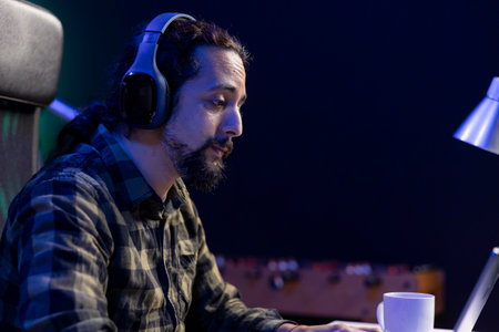 Focused man with wireless headset is attending video call meeting with clients on portable computer. Male individual with sad expression is working remotely, using laptop and headphones.の写真素材