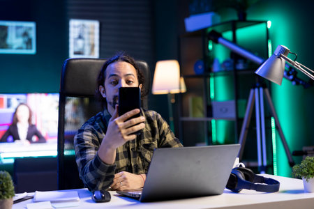 Portrait of a young man using his mobile device to communicate with friends while seated in front of...