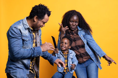 Playful african american parents and their young son having fun on camera, adorable little baby boy playing around with a tv remote control. Happy energetic family enjoying time together.の写真素材