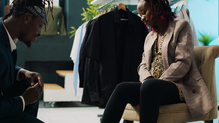 African american store employee helping woman to find the right shoe size, pregnant customer looking to buy comfortable footwear from local shopping center. Client trying on winter boots. Camera A.の写真素材
