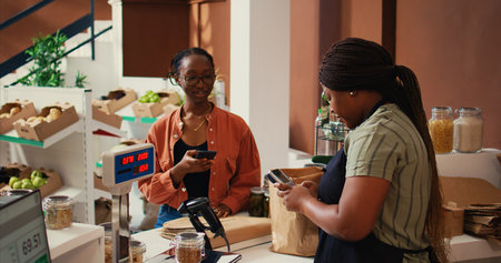 Client using nfc payment at pos to buy eco products, visiting local farmers market to restock pantry essentials. Vegan woman paying with mobile phone at checkout, nonpolluting goods. Handheld shot.の写真素材