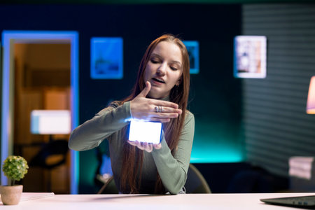 Gen Z girl in home studio using camera to capture live broadcast, reviewing mini RGB lights. Content...