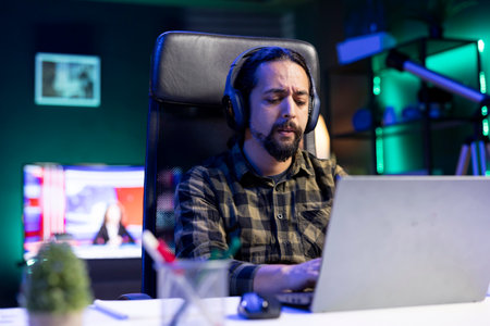 Male college student wearing wireless headphones and surfing the net on digital laptop. Freelancer working from home on portable computer while listening to music on headset.の写真素材