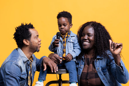Happy african american small kid singing on a microphone in studio, his mom and dad are dancing on his melody and bonding together. Proud parents having fun with their adorable young boy.の写真素材
