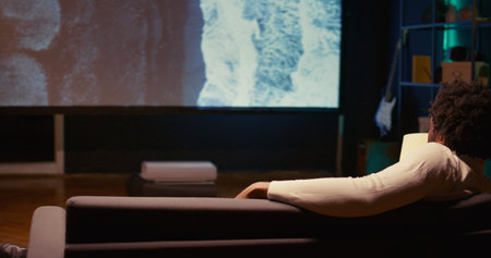 Zoom in on man mesmerized by nature documentary with beautiful cinematography on modern TV. Person enjoying seaside landscape scenery shots presented on VOD travelling channel, panning shotの写真素材