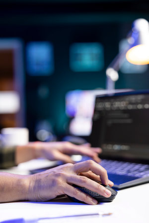 Closeup of person coding at his desk, typing on digital laptop and using a mouse, managing database...