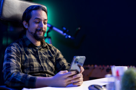 Positive male student sitting at the desk using his mobile device to browse social media. Smiling...