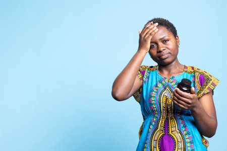 African american woman suffering from a serious migraine, reading label of pills bottle to take...