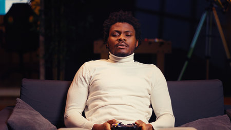 BIPOC player playing videogames on console late at night, struggling to stay awake on couch. Gamer...
