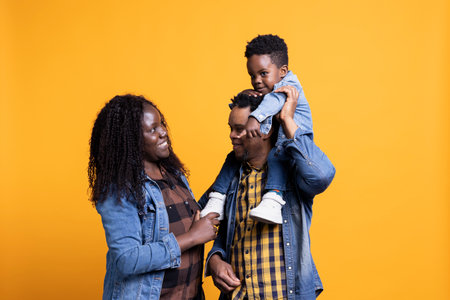 Sweet happy family with a small toddler posing in front of the camera, father carrying his son on his shoulders in studio. Parents feeling grateful for their baby boy.の写真素材
