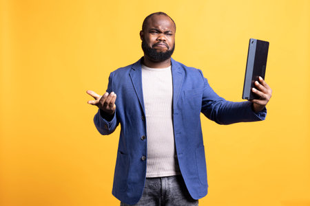Man dismayed by things said by friend during teleconference meeting using tablet, studio background. Person cringing, disagreeing with mates during videocall on portable deviceの写真素材