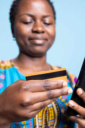 Young person entering card numbers and details to finish electronic payment, doing online shopping on smartphone. African american woman being happy after paying for clothes on web store.の写真素材