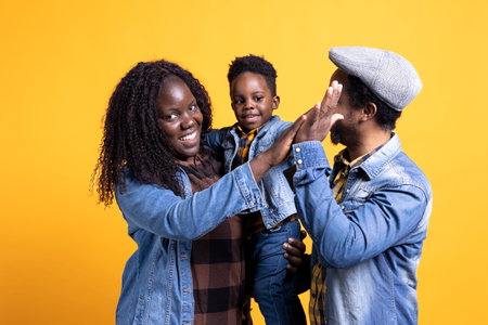 Smiling young family sharing a high five against yellow background, feeling positive and showing...