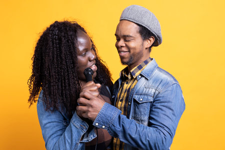 Cute husband and wife singing a romantic song on microphone in front of the camera, feeling happy and confident with their voices. African american couple in love make dedications.の写真素材