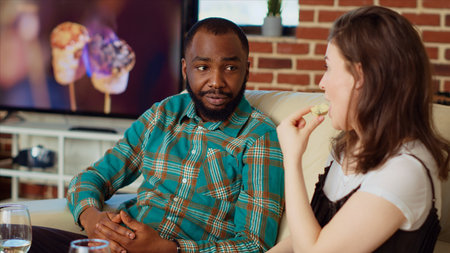 African american man chatting with girlfriends on couch at apartment party, enjoying conversation....