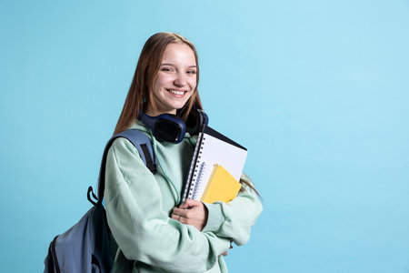 Portrait of happy teenager smiling while wearing rucksack, holding school notebook and notes, isolated over studio background. Jolly student with school supplies in arms preparing to go to collegeの写真素材