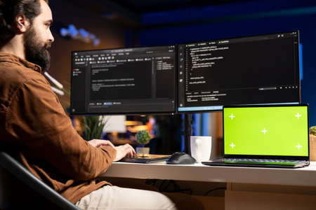 IT specialist working from home using green screen laptop, testing and deploying programs and systems. Programmer checking code displayed on computer monitors using mockup notebookの写真素材