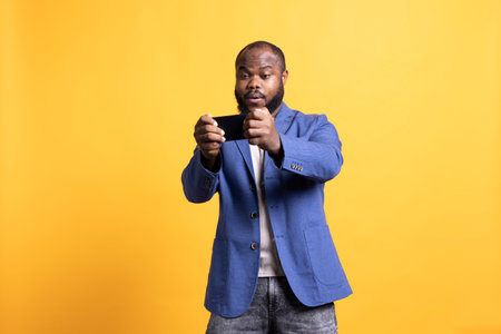 BIPOC man playing intense singleplayer videogames on smartphone, enjoying hobby. African american gamer enjoying entertaining interactive game on phone, having fun, studio backgroundの写真素材