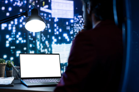 Legal investor works with white display on pc at posh workstation, admiring metropolis view at night. Chief director examining isolated blank screen on laptop, works on business expansion plan.の写真素材