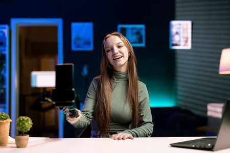 Joyous teenager using cellphone attached to selfie stick to film content for her audience, talking about gen Z topics. Upbeat influencer recording vlog for internet channel with phone cameraの写真素材