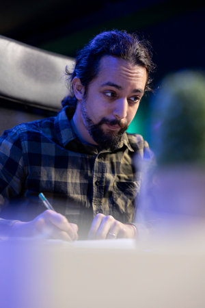 Closeup of male freelancer writing new information from laptop on his notebook. Focused man holding a pen, taking notes while researching on the internet and reviewing documents.の写真素材